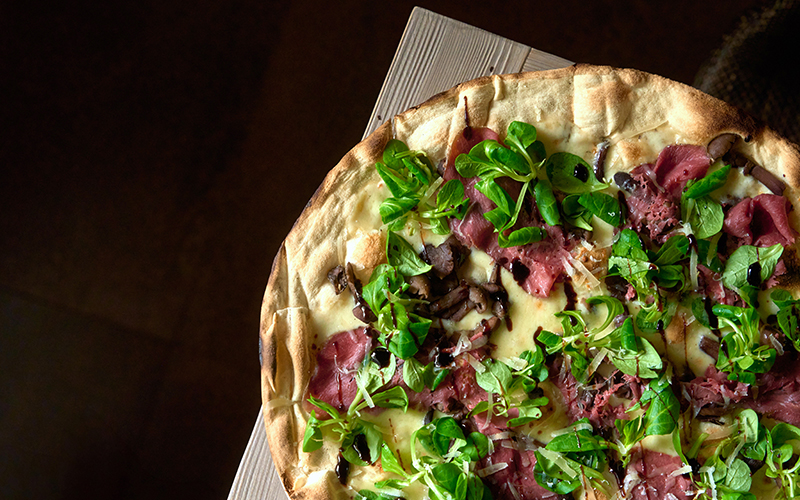 pizza bianca toerle della pizzeria da tata con fiordilatte, carpaccio di cervo, chiodini freschi, scaglie di Asiago DOP Grün Alpe mezzano, glassa di aceto balsamico al lampone, valeriana.
